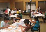 複数の子どもたちがテーブルを囲んで座り、まが玉作りに熱心に取り組んでいる様子の写真