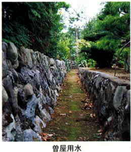 緑の木々の下にある、石垣に囲まれた、底に苔が生え、落ち葉がたまった用水路の写真の下に「曽屋用水」と書かれた画像