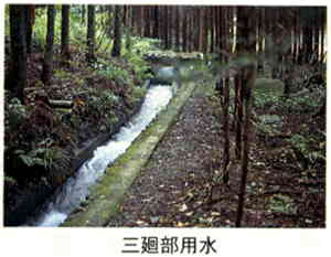 林の中にある細い用水路を水が勢いよく流れている様子の写真の下に「三廻部用水」と書かれた画像
