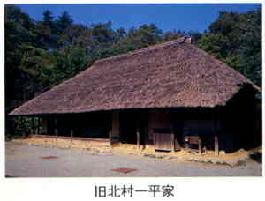 林を背後に建つ、木造藁ぶき屋根の平屋の旧北村一平家の外観写真