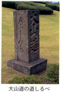 美しく整備された芝生の広場に「大山道」などの文字が彫られた直方体の石碑「大山道の道しるべ」が建っている写真