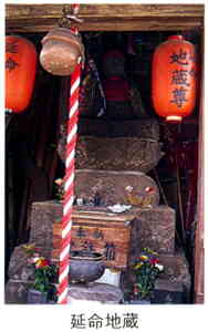 両脇に「地蔵尊」と書かれた朱色の提灯が吊るされている木造の祠の中で、石造りの土台の上に延命地蔵が鎮座している写真