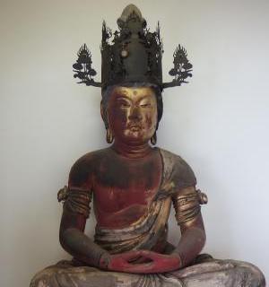 顔や体の一部に金箔が残り、摩耗で赤や黒い色露出した、精巧な黒い冠を戴いた木造の仏像が、両手を膝上で組む定印を結んで結跏趺坐している木造大日如来坐像の写真