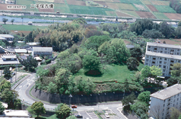 川の側の住宅街に囲まれた道路の中央に位置する二子塚古墳を空から撮影した航空写真