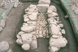 土を掘り下げた遺跡の発掘現場に、大小の石が通路と部屋のように積み上げられた、金目原遺跡第3号墳とされる遺構の写真