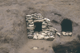 土でできた壁面に石を積み上げた入口を持つ横穴墓が写し出されており、その隣にも同様の横穴がある、遺跡のクローズアップ写真