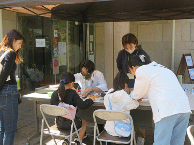 建物の入り口前に設置された受付で、2人の女の子が用紙に記入をしている様子の写真