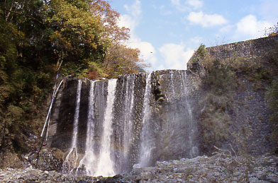 周囲は紅葉を始めた木々とゴロゴロした石で覆われた河床が広がり、人工的に作られた石積みの巨大な堰堤から、水が均一なカーテンのように勢いよく流れ落ちている写真