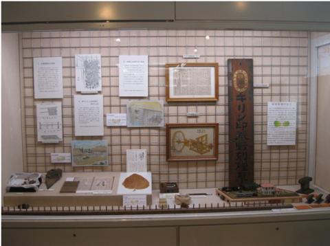 さまざまな資料や模型がガラスケース内に展示されており、壁にはパネルや古い木製の看板がかけられている、展示スペースの写真
