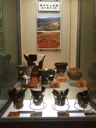 縄文土器の破片や修復された土器が、発掘当時の様子を写した写真も添えられて、ガラスケースの中に並べて展示されている写真