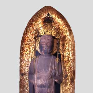 金色に輝く炎のような唐草模様の光背を背景に、頭には華やかな宝冠を戴き、右手をやや持ち上げた姿で濃い茶色をした仏像が直立している姿を正面から写した写真