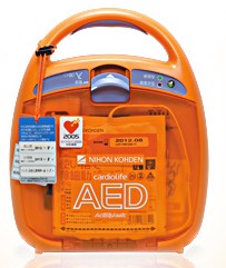 オレンジ色の筐体に取っ手が付き、正面に操作パネルと複数のラベルが貼られた日本光電工業製の自動体外式除細動器AEDの写真