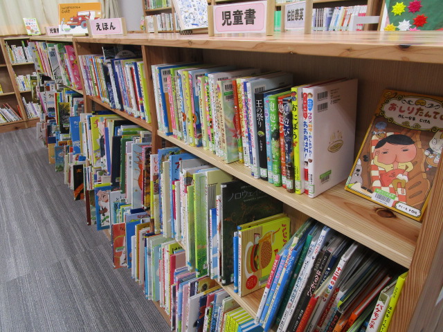 木製の本棚に児童書と書かれた白い札が立ち、カラフルな表紙の絵本や児童書が複数段にわたって並ぶ図書館の児童コーナーの写真