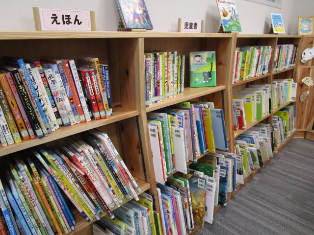 木製本棚にえほんと児童書の白い分類札が立ち、カラフルな絵本や児童書が複数段にわたって整然と並ぶ図書館の児童書コーナーの写真