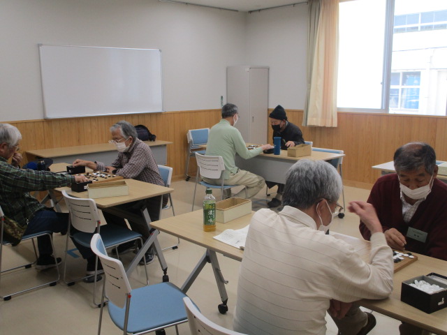 教室の中で囲碁の盤を囲んで複数の人が座り、講師の指導を受けながら囲碁の勉強をしている様子を写した、囲碁学習会の写真