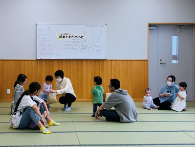 畳の部屋で、白いボードの前に座っている人が子供と話しており、周囲には複数の大人と子供が座っている様子を写した、親子参加型講座の写真