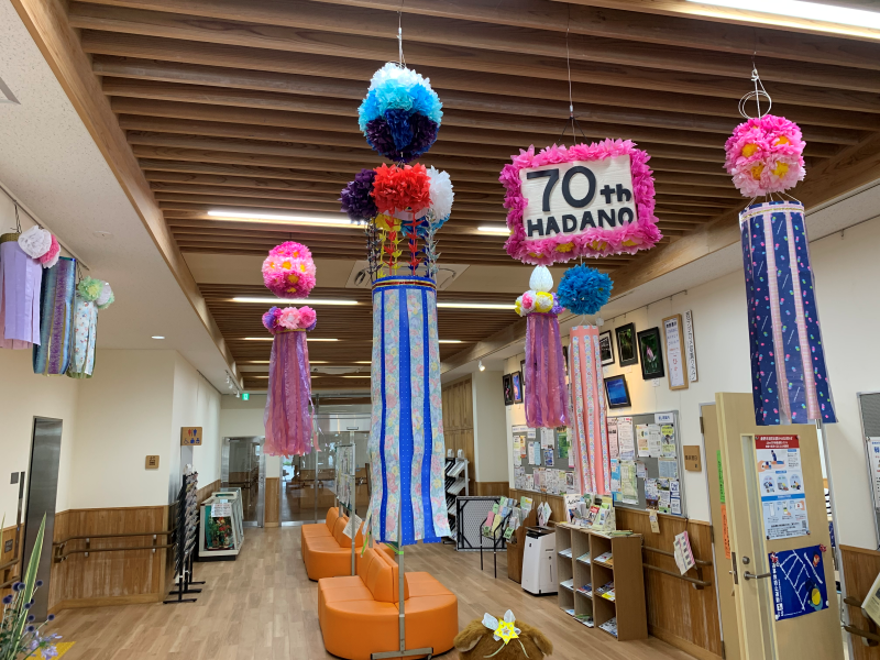 木目調の天井とフローリングの広々とした屋内空間に、ピンクや青などの色鮮やかな七夕飾りがいくつも吊り下げられた写真