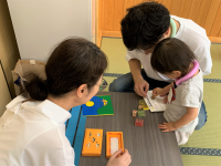 畳の部屋で、子どもが父親に手伝ってもらいながら机の上でカードにスタンプを押す様子を上方から捉えた写真