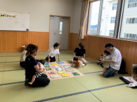 畳の部屋で数組の親子が集まり、中央に広げられた色とりどりの絵本やカードのような教材を使いながら、大人が子どもに何かを教えている学習会の様子の写真