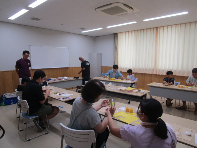 広々とした室内で、大人と子どもが複数参加し、創作活動に取り組むワークショップの様子を捉えた写真