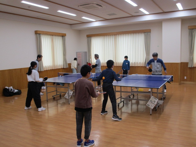 室内で、手前の2台の卓球台を使い、子供や高齢者を含む複数人が、世代を超えて卓球を楽しんでいるスポーツ交流イベントの様子を捉えた写真