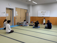 畳敷きの広い部屋で、数人の女性が幼い子どもを抱っこして床に座って向き合い、手あそびをしている写真