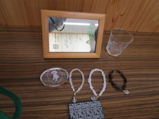 木目調のテーブルの上に、木製のフレームの鏡、グラス、トイプードルのイラストが描かれた透明な楕円形のプレート、そして3本の天然石ブレスレットが並べられている、手芸作品などの展示写真