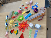 明るい木目のテーブルの上に、星、花、動物などをかたどった色鮮やかな折り紙や紙の工作物が多数広げられており、七夕飾りや祭りの飾り付けのような手芸作品を集めて上から撮影した写真