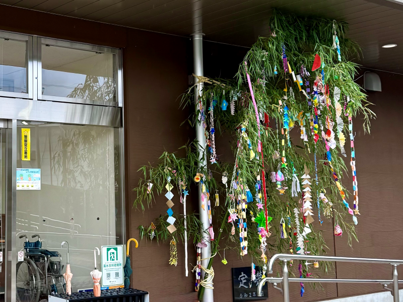 建物の出入り口付近の柱に、色とりどりの短冊や飾りが大量につけられた笹の葉が立てかけられている写真