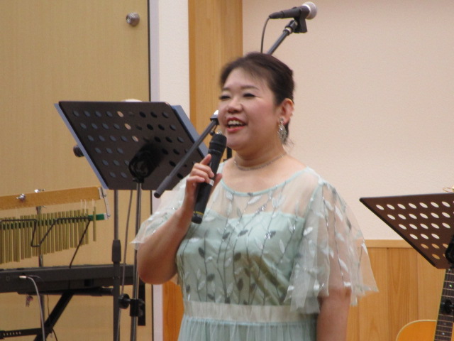 淡いミントグリーンのドレスを着た女性が、マイクを持って笑顔で歌っている様子を捉えた写真