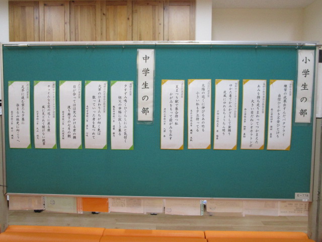 緑色の掲示板に「小学生の部」と「中学生の部」に分かれて、数枚の川柳の入賞作品が短冊に縦書きで貼られている写真
