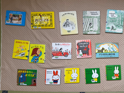 薄茶色のキルト布のような敷物の上に、「ねむたいひとし」、「ぐりとぐら」シリーズ、「ミッフィー」シリーズなどの様々な絵本や児童書が合計15冊並べられている様子の写真