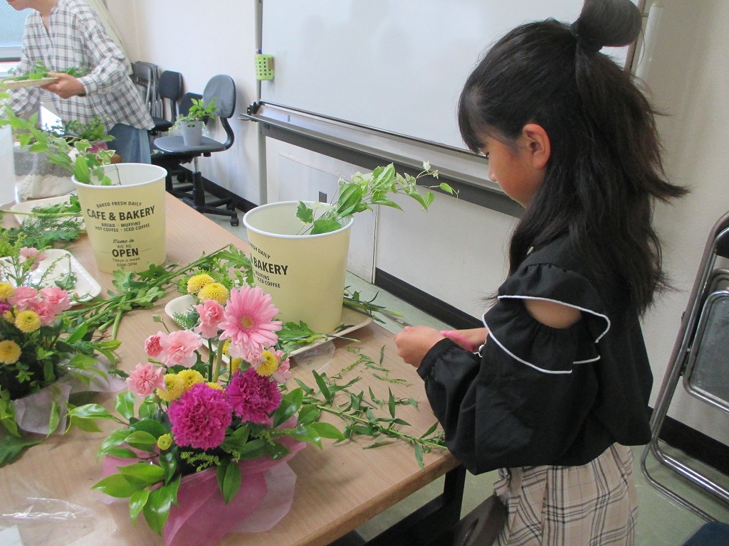 テーブルで色とりどりの花材を使ってフラワーアレンジメントを製作している女の子を横から撮影した写真
