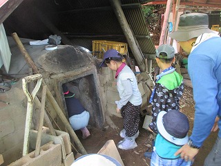 帽子をかぶった子供たちが好奇心旺盛に窯の中を覗き込み、大人がその様子を見守っている写真