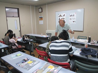 教室内で昆虫のポスターが貼られたホワイトボードを背に、男性講師が机に向かっている親子に丁寧に説明しながら昆虫に関する工作や観察学習を行っている様子の写真