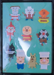 黒い額縁に入れられ緑色の台紙に貼り付けられた、複数の折り紙作品が整然と並んでいる展示物の写真