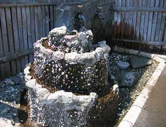 竹垣を背景に、複数の岩と玉砂利で3段に積み上げられた円柱形の人工の井戸の写真