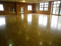 フローリング張りの広い室内で多数の窓があり、壁に大きな鏡が設置されている多目的ホールの写真