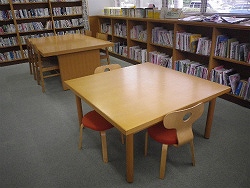 児童書の棚に囲まれたスペースに、子供用の椅子とテーブルが2セット置かれており、落ち着いた雰囲気の図書室の室内を写した写真