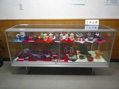 ガラスケースの中に、小さな人形や、陶芸の作品が展示されているの写真