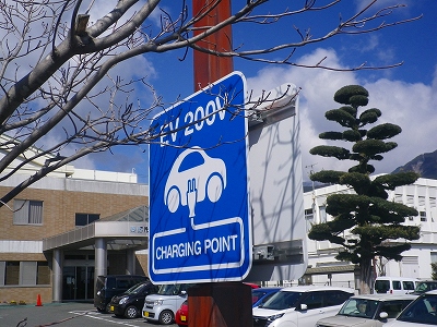 駐車場に設置された「EV 200V」「CHARGING POINT」の文字と車の絵が書かれた、電気自動車の充電スポットの青い看板の写真