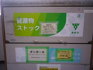 資源ごみの回収ボックスに「資源物ストック」という大きな文字や、秦野市のロゴマーク、ダンボールの分別に関する案内が貼られている写真