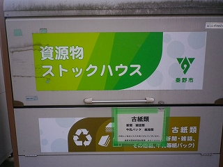 資源ごみの回収ボックスに「資源物ストックハウス」という大きな文字と、秦野市のロゴマーク、古紙類の分別に関する案内が貼られている写真