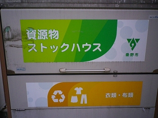 資源ごみの回収ボックスに「資源物ストックハウス」という大きな文字と、秦野市のロゴマーク、衣類・布類の案内が貼られている写真