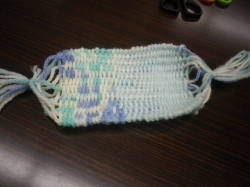 木目調のテーブルの上に置かれた、水色と白色と紫色の毛糸で手織りされた四角いコースターの写真