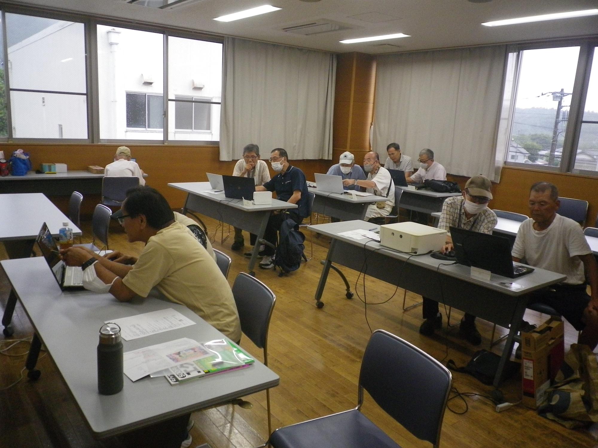 木目調の床と大きな窓のある教室で、参加者たちが机に向かって各自のノートパソコンを操作し、熱心にパソコン講座に取り組んでいる様子の写真