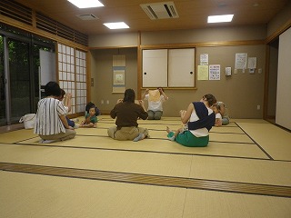 和室の畳の上で、数組の親子が輪になって座り、ハンカチを広げて持ち遊んでいる写真