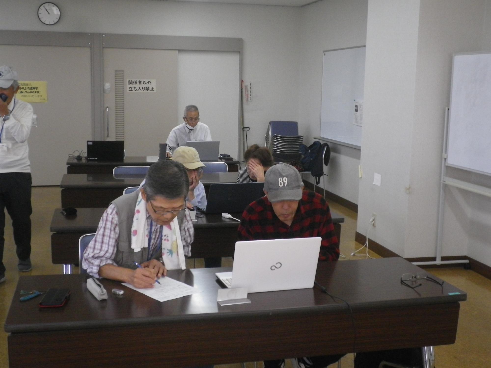 教室で、数名の参加者が各自のノートパソコンに向かって集中して作業に取り組んでおり、手前の男性は資料に書き込みをしているパソコン教室の写真