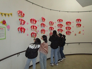 複数の少女たちが白い曲面の壁に飾られた、ひな人形やピンクの星形の飾り付けを、身を乗り出すようにして見上げている様子の写真