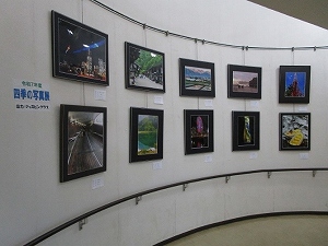 半円を描くような白い壁に沿って、夜景、街並み、自然風景など、さまざまなテーマの額装された写真が二段に渡って十数点展示されているギャラリー内の写真